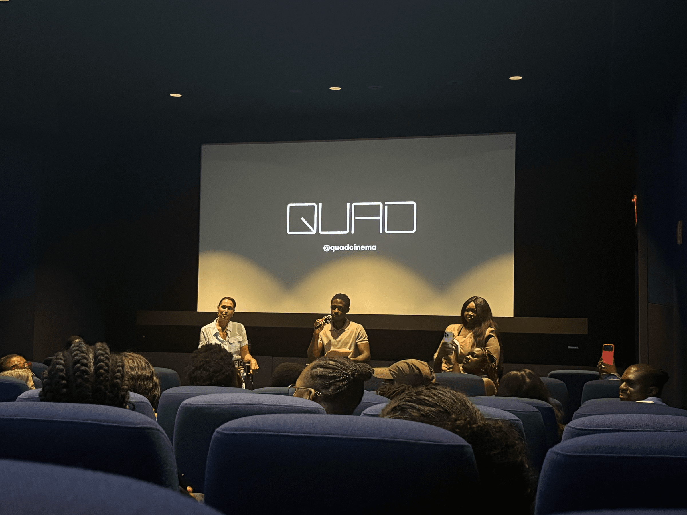 A conversation on stage at Quad Cinema, with the Quad screen behind the speakers and the audience seated in front.